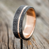 Shown here is "Vertigo", a custom, handcrafted men's wedding ring with an offset 14K gold inlay with a hammered, fire-treated, black zirconium overlay on a 14K gold band, upright facing left. Additional inlay options are available upon request.